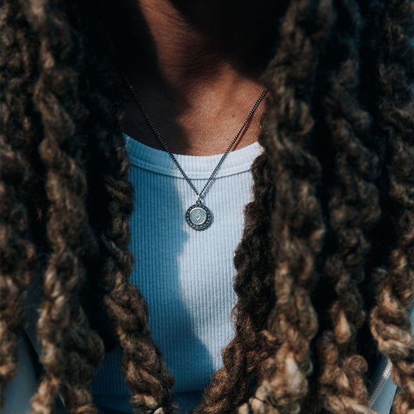 Close up of model with long dread locks wearing a white top and a silver pendant necklace