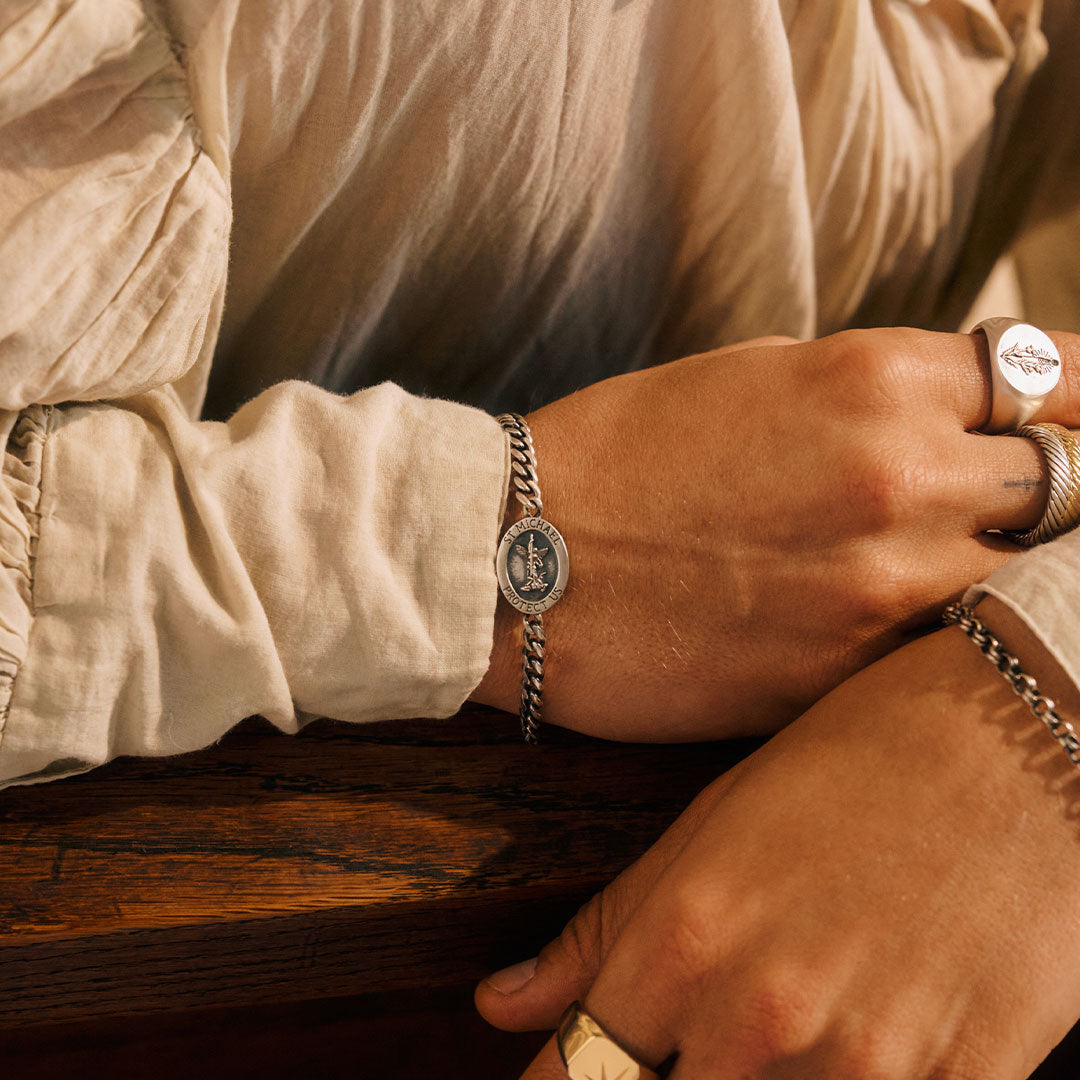 Close-up of a person's wrist with a bracelet and ring, wearing a beige shirt.