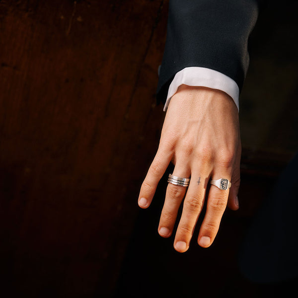 Hand wearing two rings on a dark background