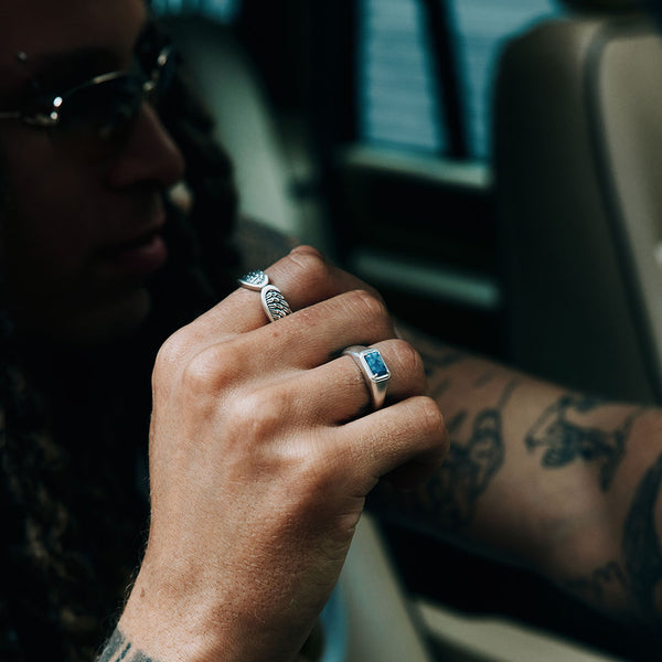 Male in a car, his hand is up wearing 2 Silver rings