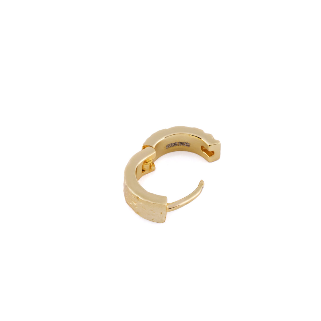 Gold huggie earring with rough texture laying on white background - Serge DeNimes