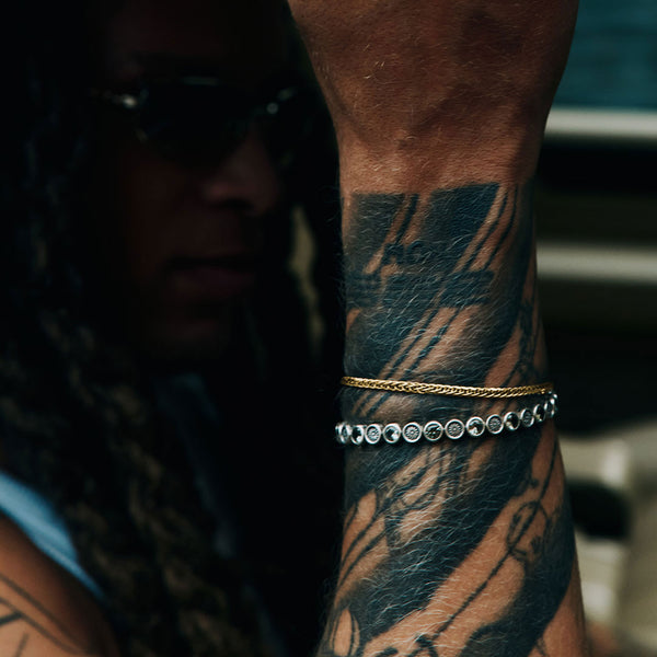 Person with tattoos wearing a gold bracelet on a blurred background