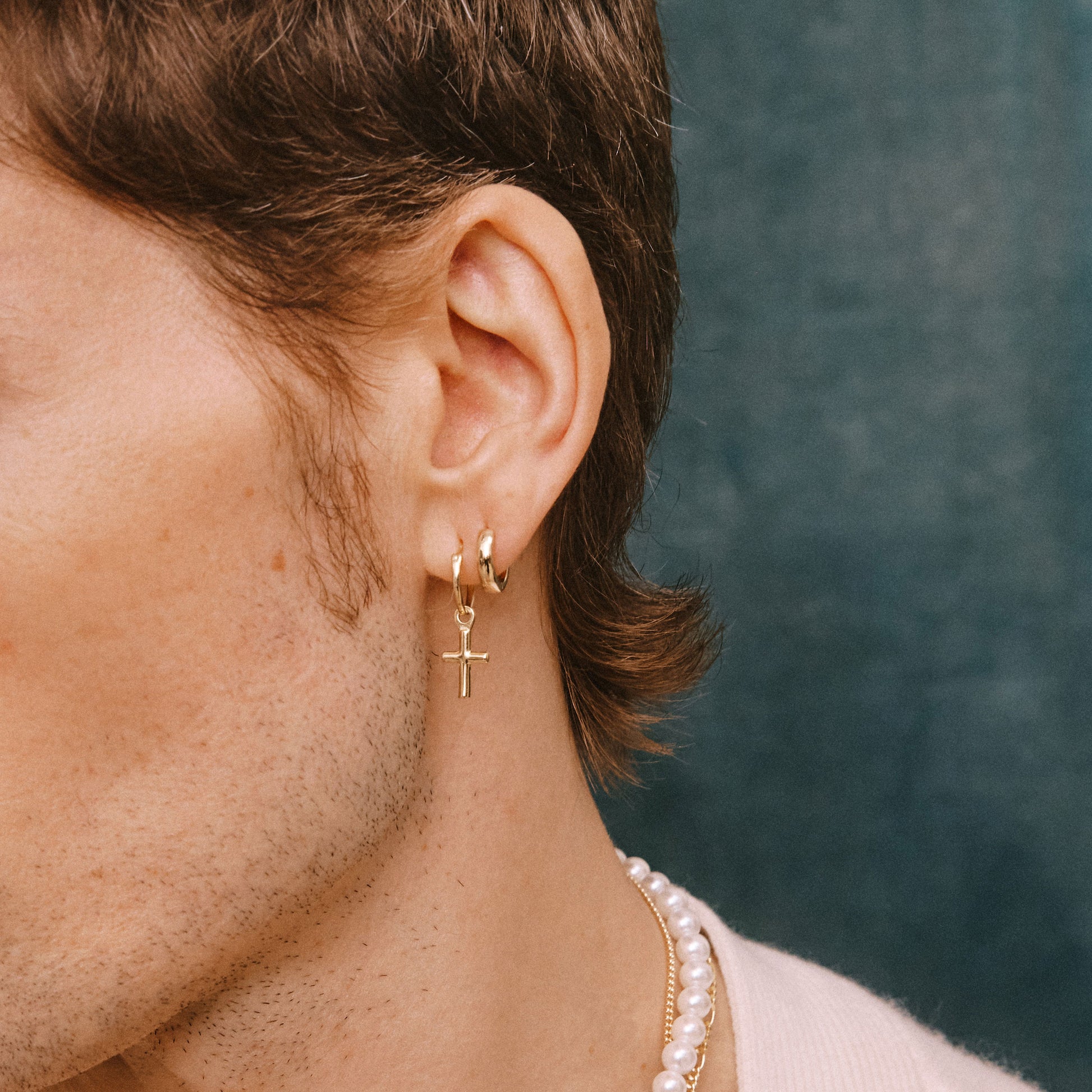 Model wears 2 gold earrings in ear lobe
