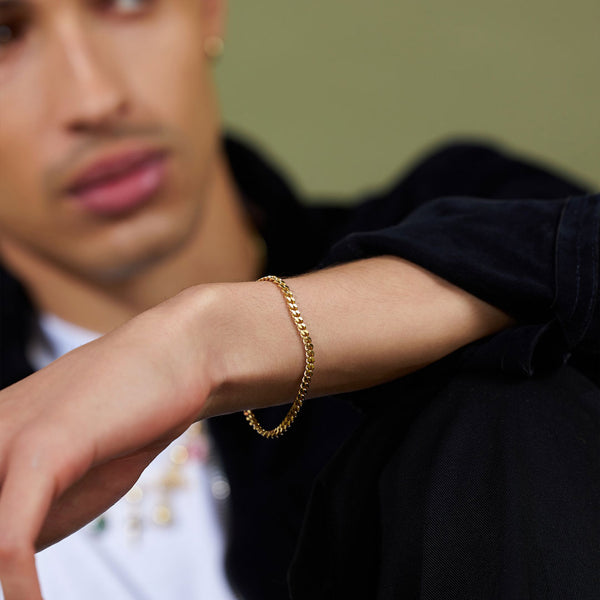 Model sits infront of a green backdrop and on his wrist he is wearing a Gold Diamond Cut Chain bracelet