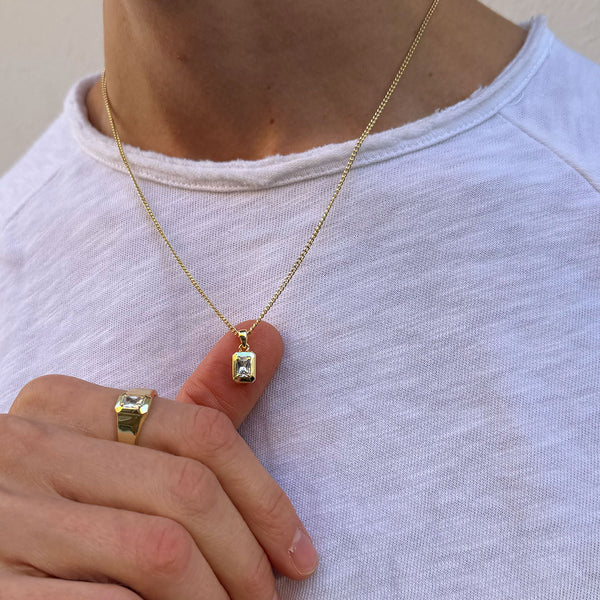 Model wears a white t-shirt and shows the Gold pendant necklace to the camera and is wearing a matching ring