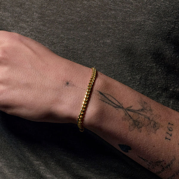 Model with tattoo's wears a gold curb bracelet on his wrist - Serge DeNimes