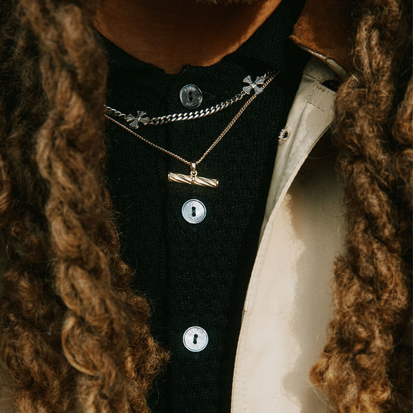 Model with long hair wearing black knitted top under 2 necklaces