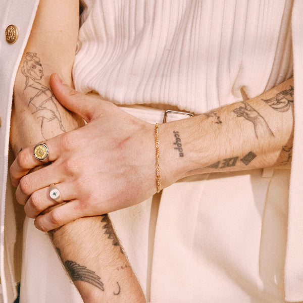 Model with tattoos wears a white outfit with a Gold Figaro Bracelet and 2 Silver rings - Serge DeNimes