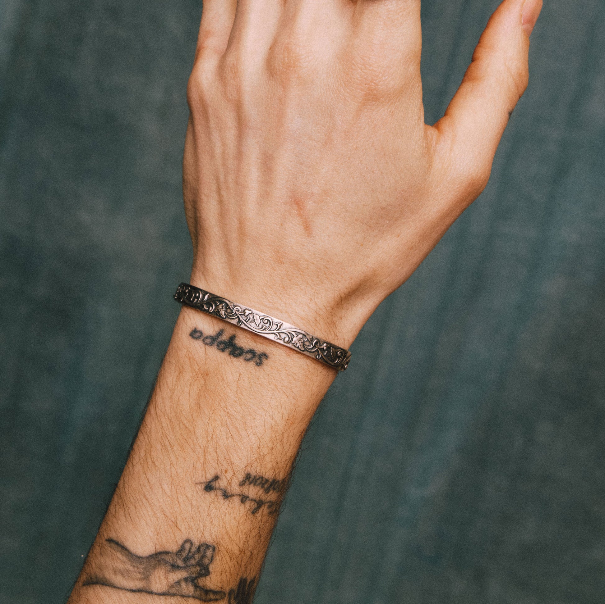 Model with tattoo'ed arm wears a Silver cuff bangle with floral detailing - Serge DeNimes