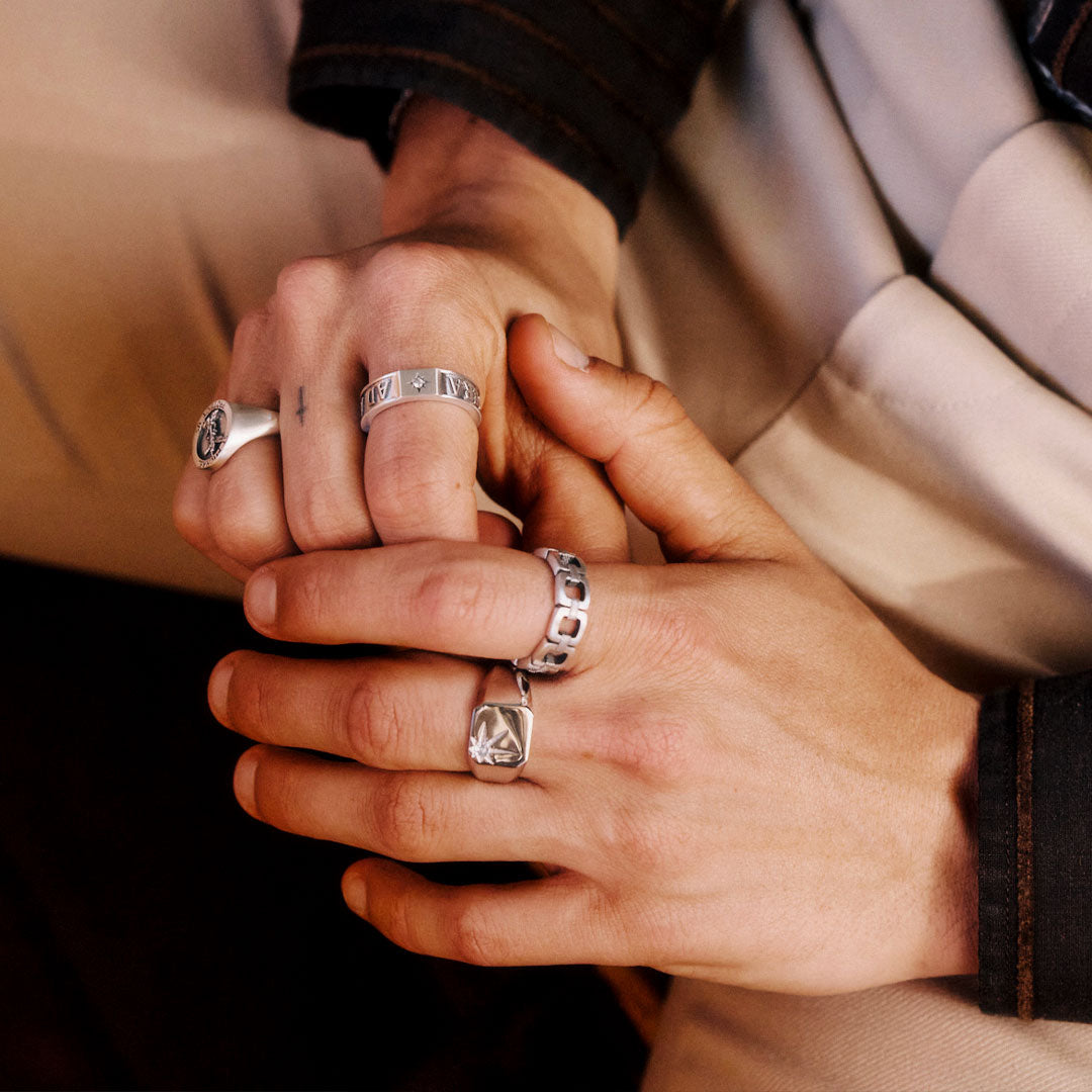 Close-up of two hands holding each other, wearing silver rings.