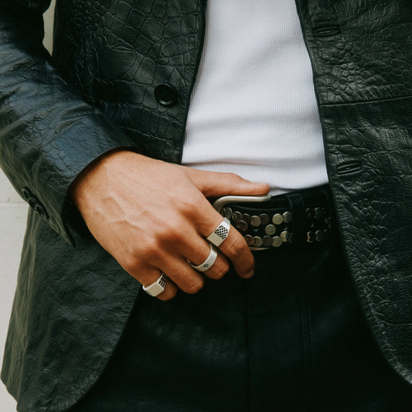 Person wearing a black leather suit holds their belt wearing multiple Silver rings