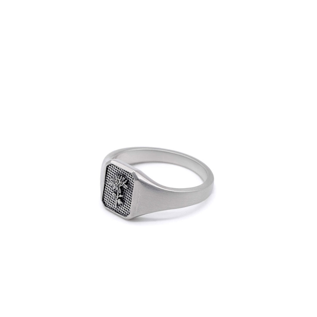 Silver ring with a flower inside a rectangle shaped face on a white background by Serge DeNimes
