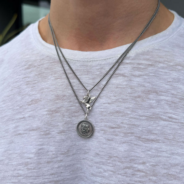 Close up of model wearing white t-shirt under 2 silver pendant necklaces