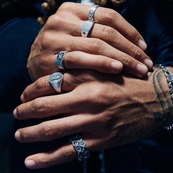 Male hands resting on eachother wearing multiple Silver Rings against a dark background