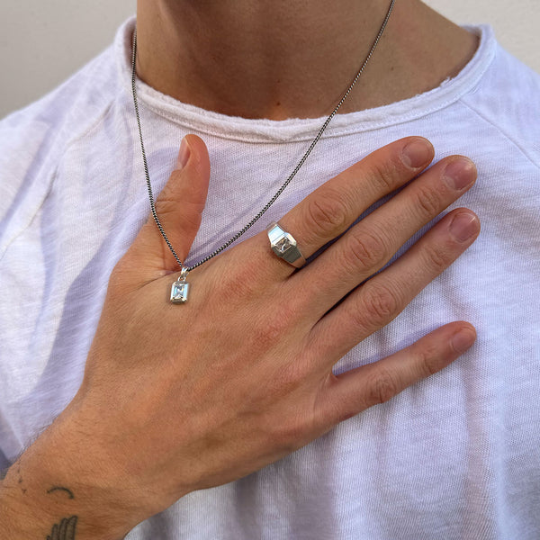 Model wears white top with hand resting on chest wearing a silver necklace and silver ring both with large clear gemstones