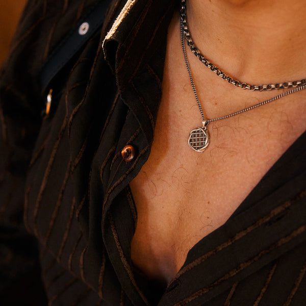 Close-up of a person wearing a necklace with a unique round pendant and a Silver chain.