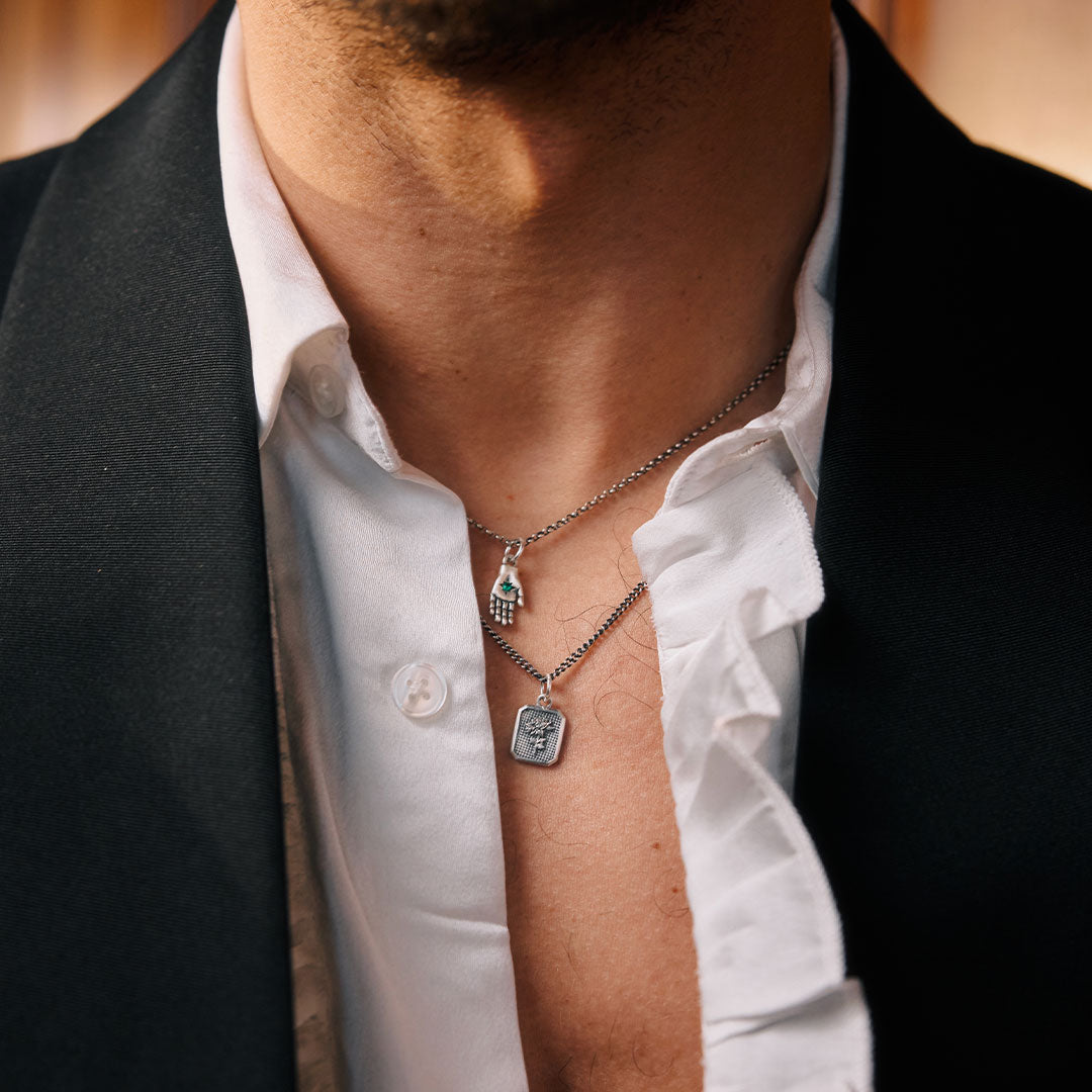 Person wearing a white shirt with two necklaces, one with a green gemstone and the other with a rectangular pendant.