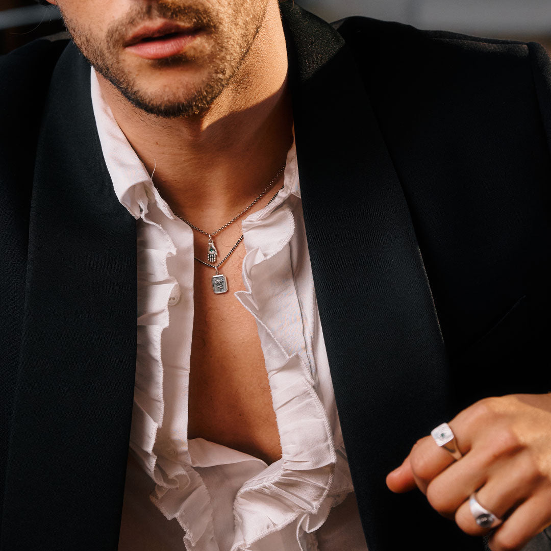 Man wearing a black blazer over an open white shirt, with a focus on jewelry.
