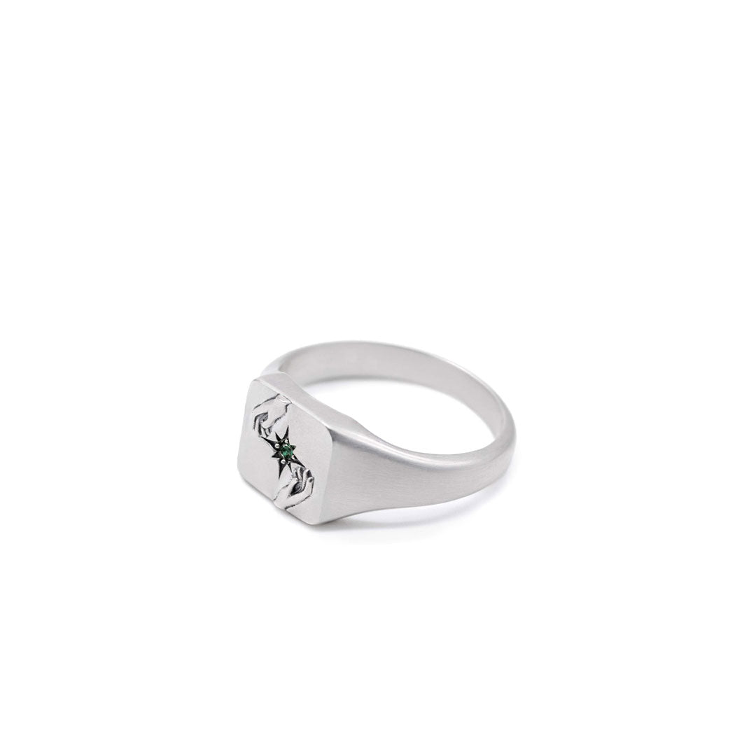 Silver ring with 2 hands reaching for a green gemstone on a white background