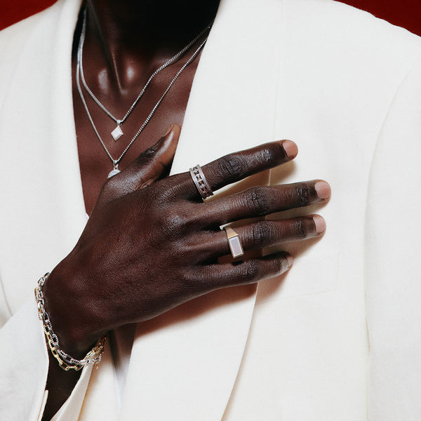 Model wears a white blazer with multiple layered necklaces, bracelets and rings