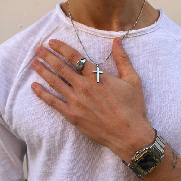 Model wears a white top with a silver cross necklace and a silver signet ring with green gemstone - Serge DeNimes