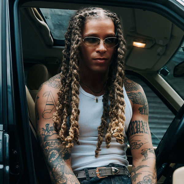 Person with braided hair and tattoos sitting inside a car