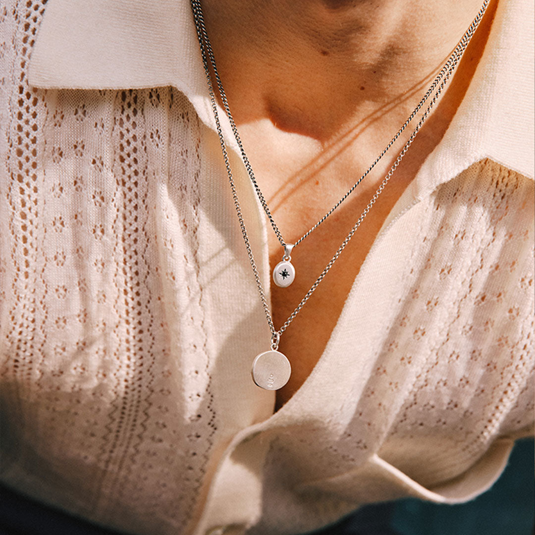 Person wearing a knitted button up shirt leans forward showing 2 pendant necklaces
