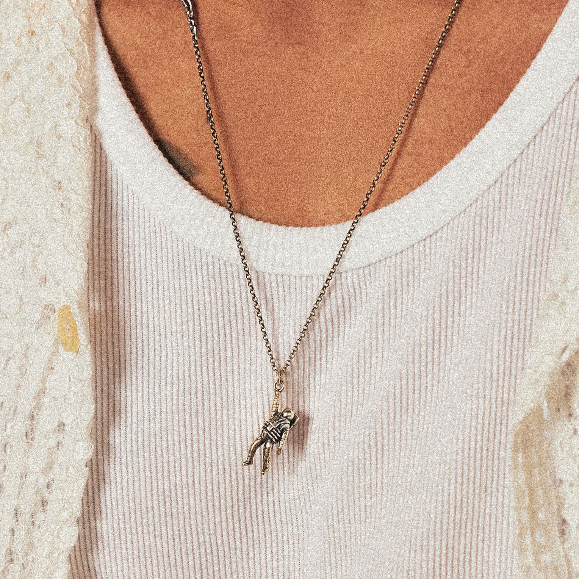 Model wears white ribbed top with a Silver necklace of an astronaut hanging onto a chain