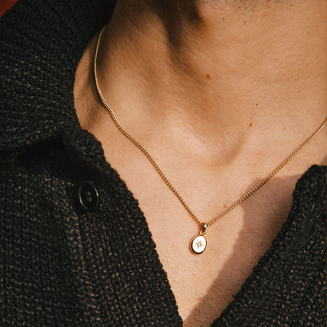 Model wears black knitted t-shirt with a gold pendant necklace at the neckline
