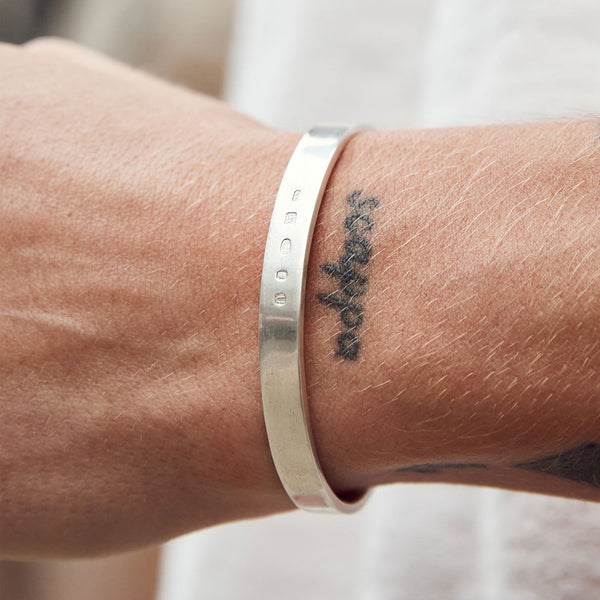 Model wrist wearing Silver flat cuff bangle with 5 hallmarks struck on the front - Serge DeNimes